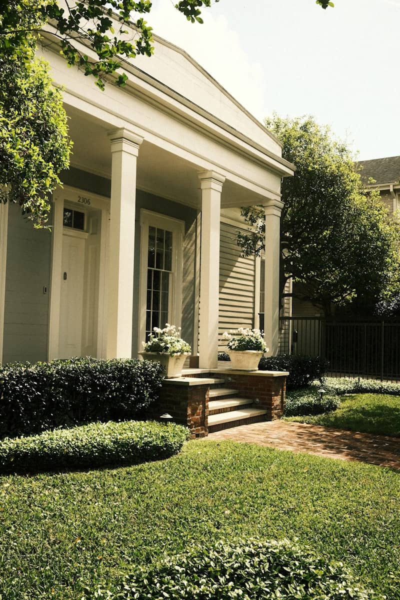 A charming house with white columns and lush greenery.