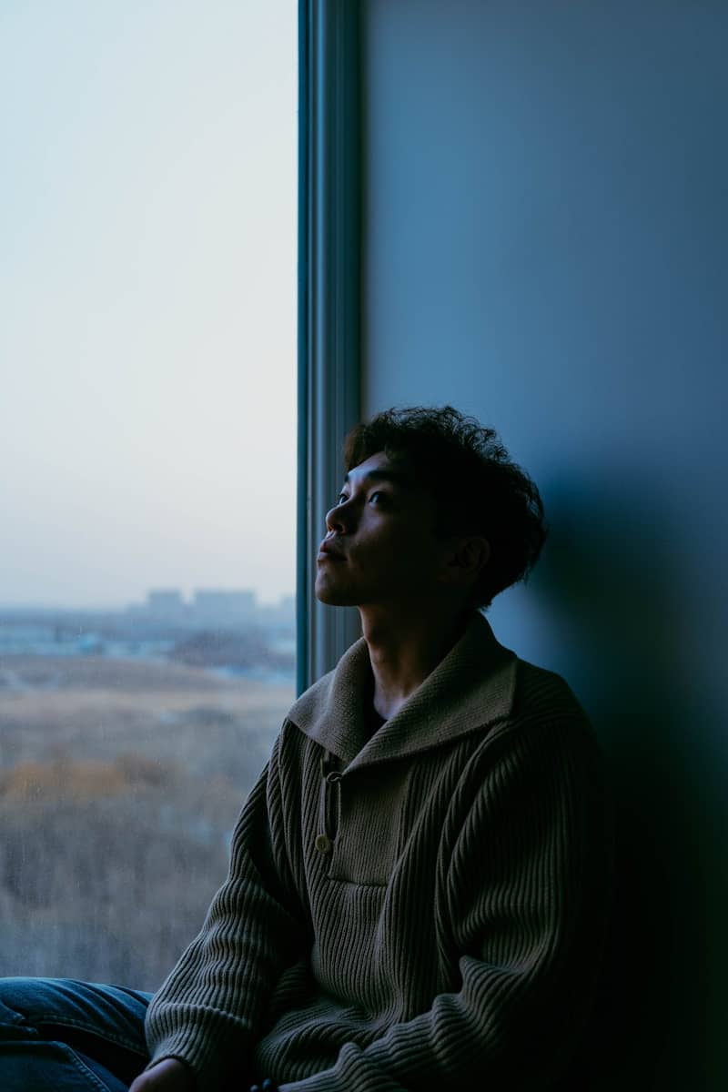 A man sitting on a window sill looking out the window