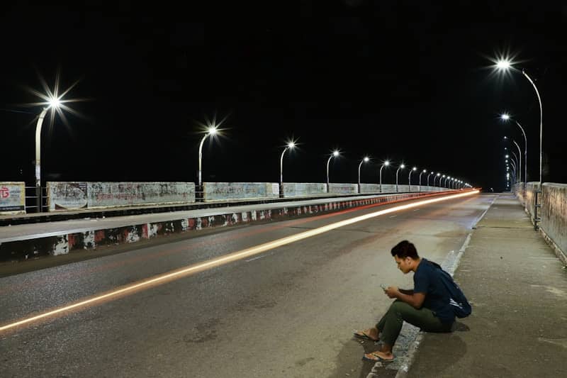 Man sitting on a bridge at night with light trails