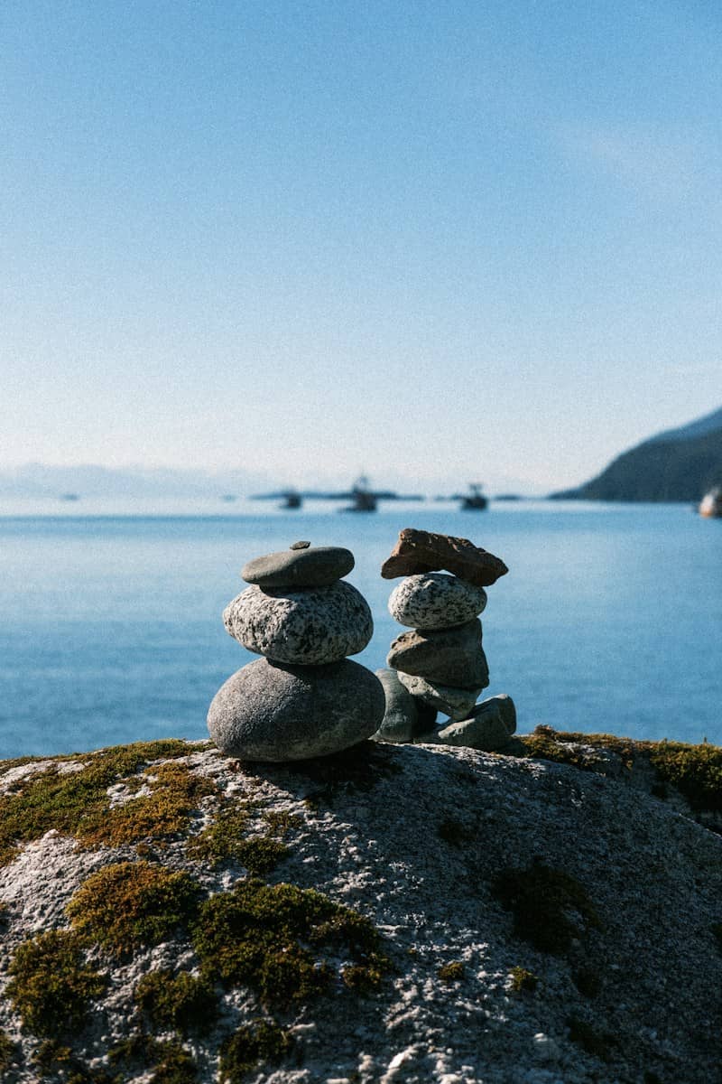 Two stone cairns on a mossy rock overlooking a calm blue bay