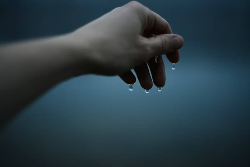 A hand with water droplets falling from fingertips against a dark blue background