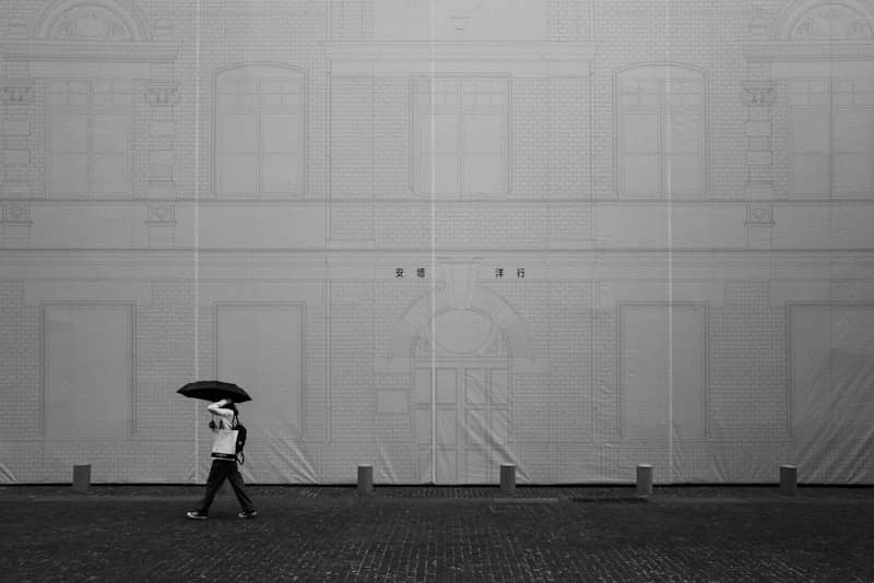 Person with umbrella walks against large building facade.