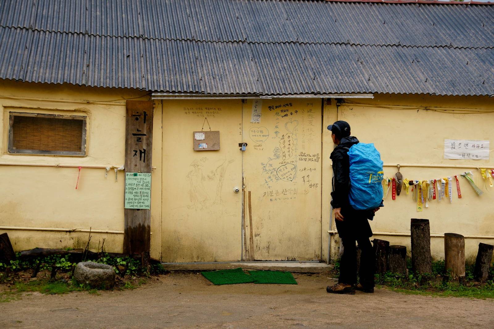 A person wearing a large blue backpack pauses in front of a closed doorway.