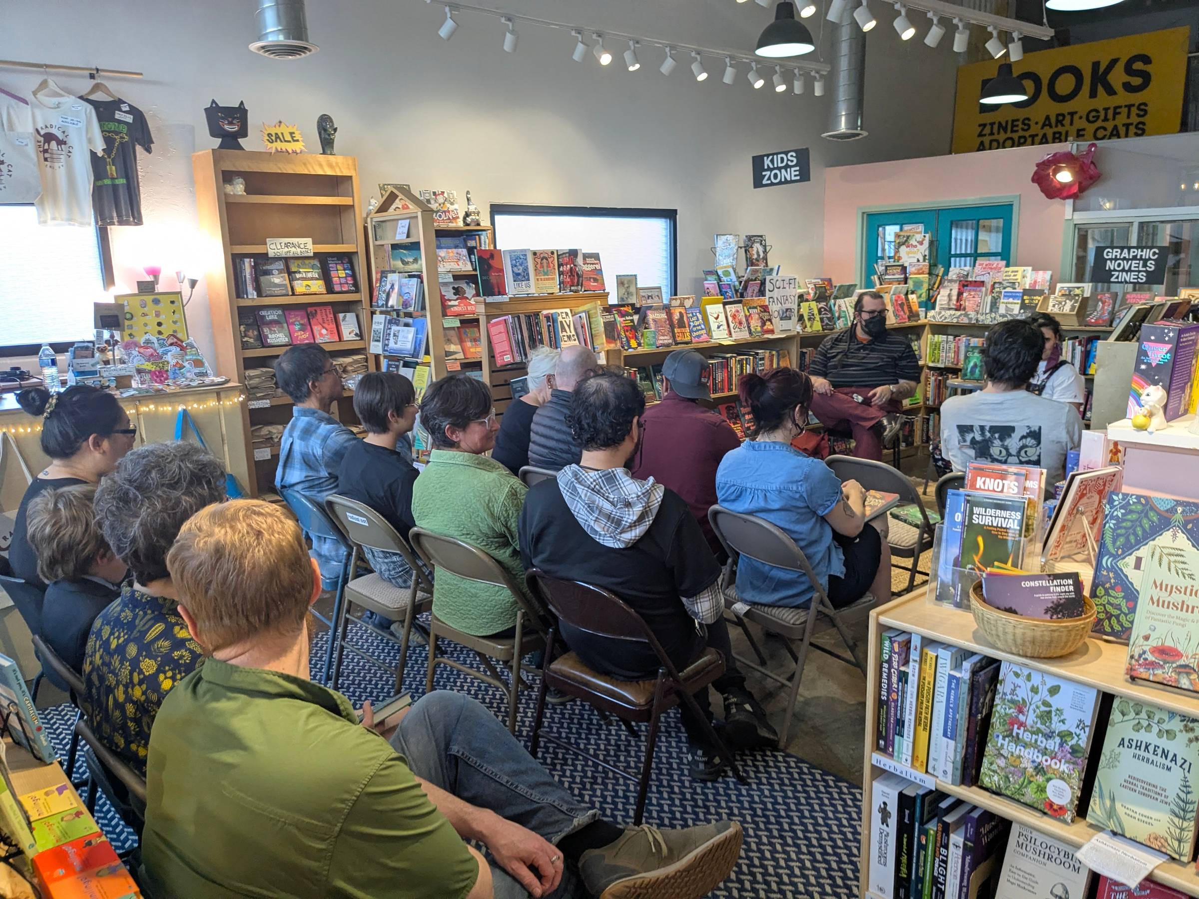 Audience sit in folding chairs in the middle of a bookstore, with the speakers (Naseem and Griffin) in front. Bookshelves box them in. This is a different angle from the earlier picture.