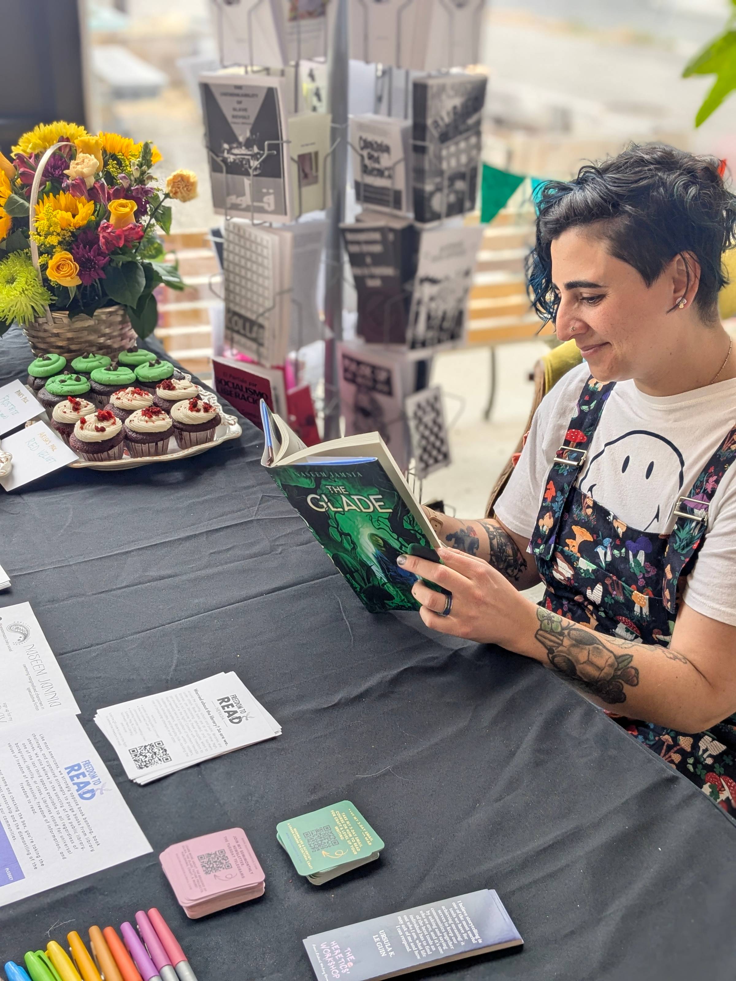 Naseem sits at a table, reading a copy of The Glade. It's a different angle from the earlier one, where papers on the black tablecloth are still visible.