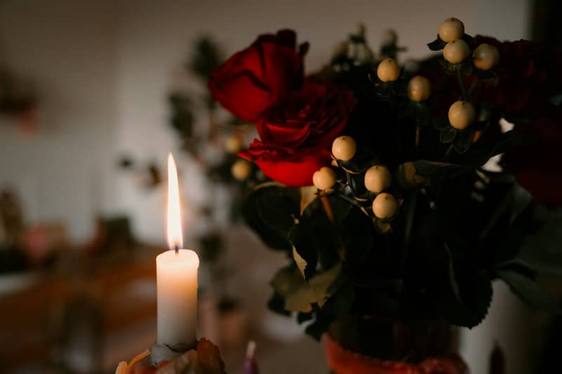 A lit candle beside a bouquet of red roses.