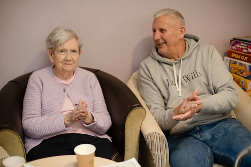 Elderly woman and man sitting in chairs clapping.