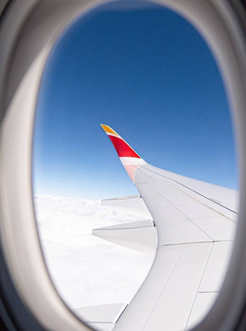 Airplane wing against a clear blue sky above clouds