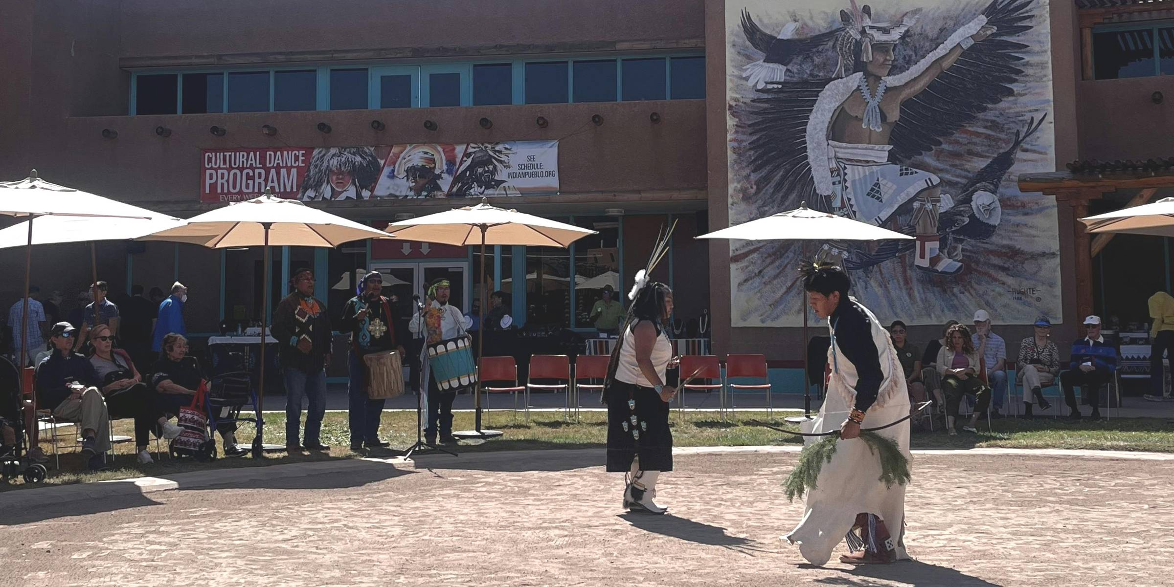 Two dancers in traditional regalia perform in a sunlit courtyard during the Cultural Dance Program at the Indian Pueblo Cultural Center in Albuquerque, NM.