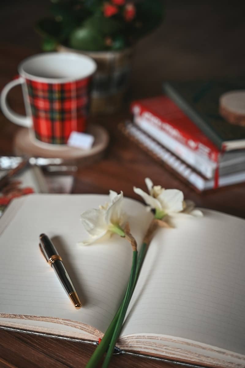 Open notebook with pen and flowers on table