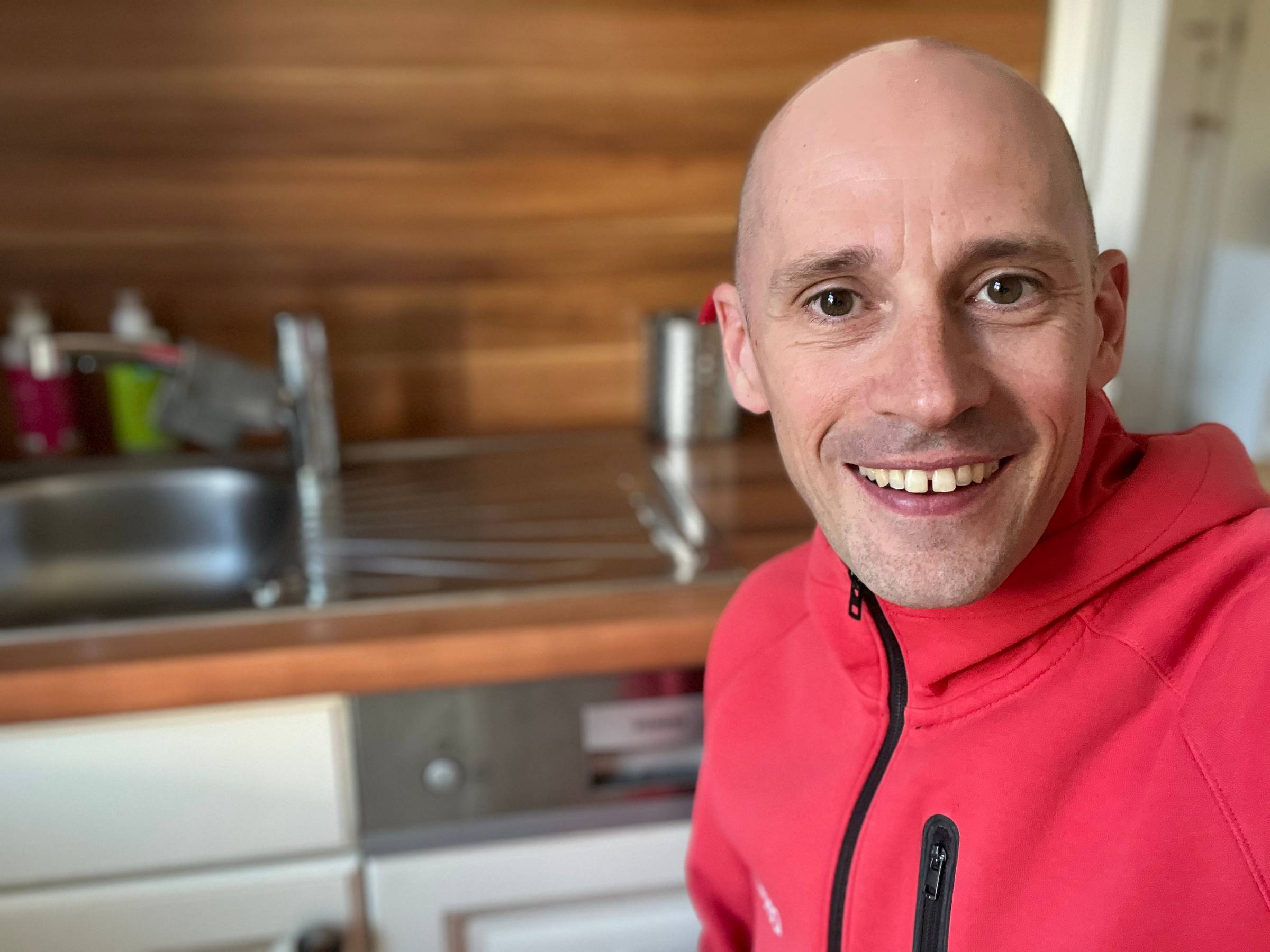 Sven smiling infront of a clean kitchen sink and dish washer