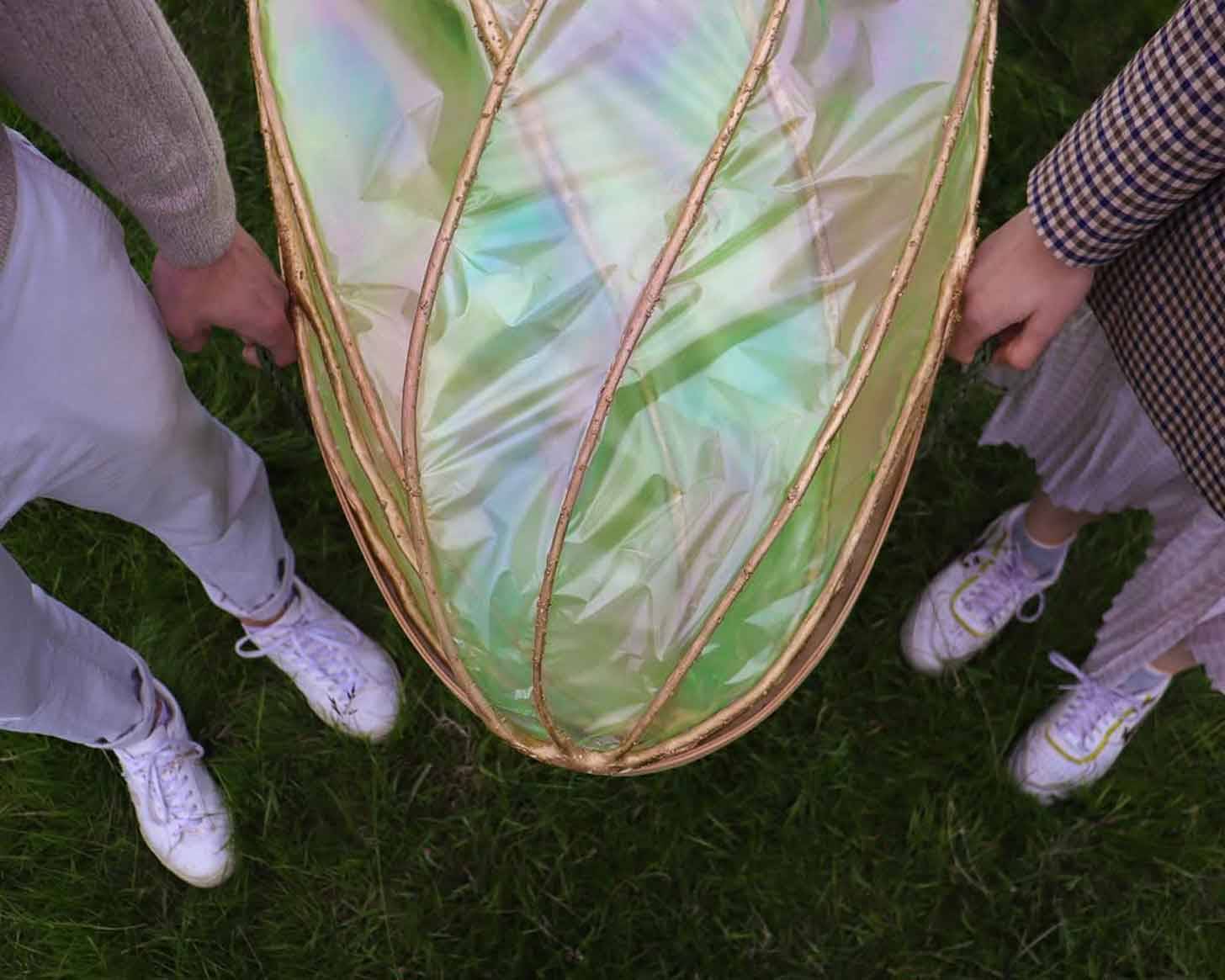 Two people holding the front of a coffin that looks like an iridescent cocoon
