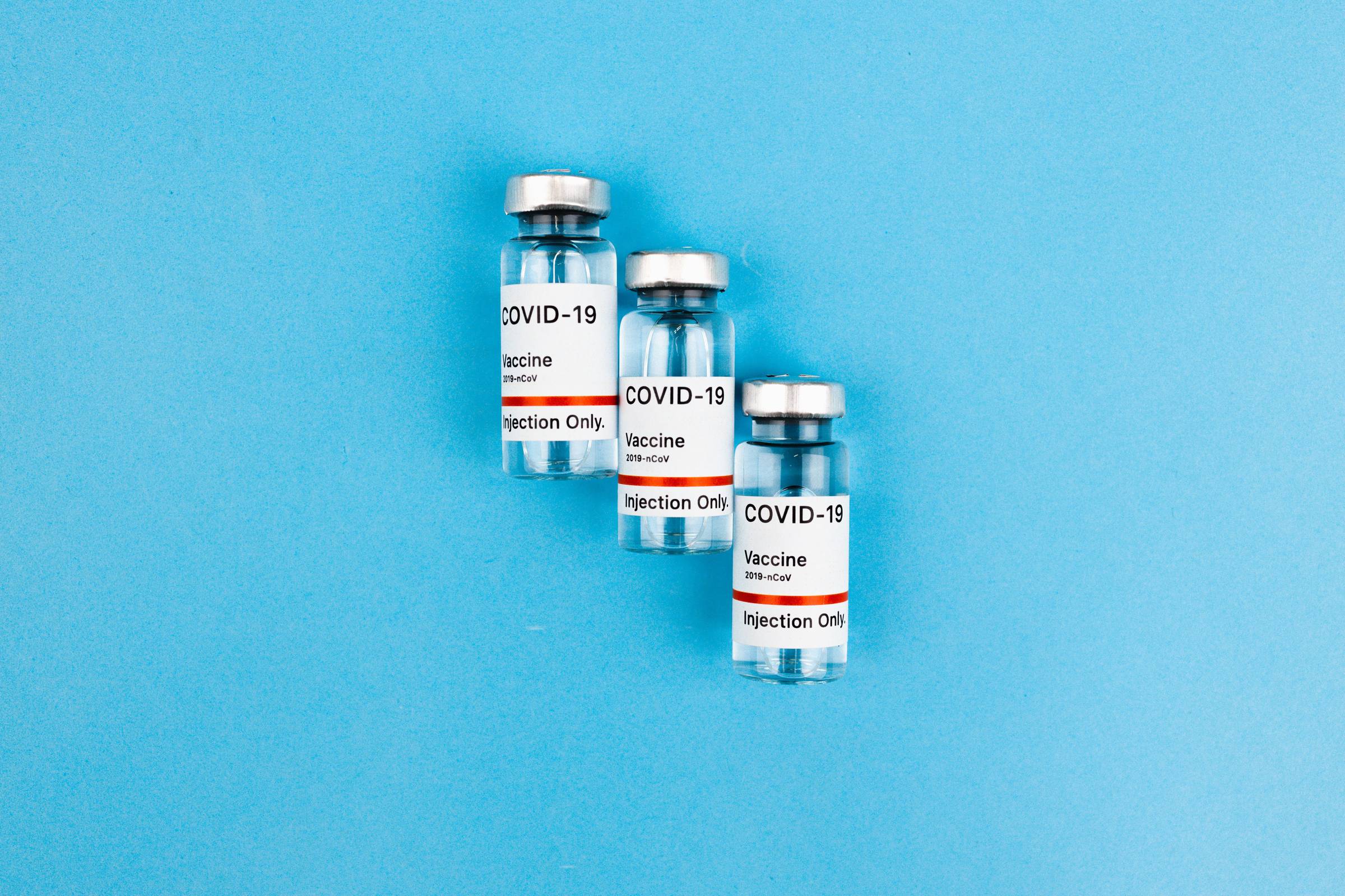 Three COVID-19 vaccine bottles labeled "injection only" side by side against a blue background