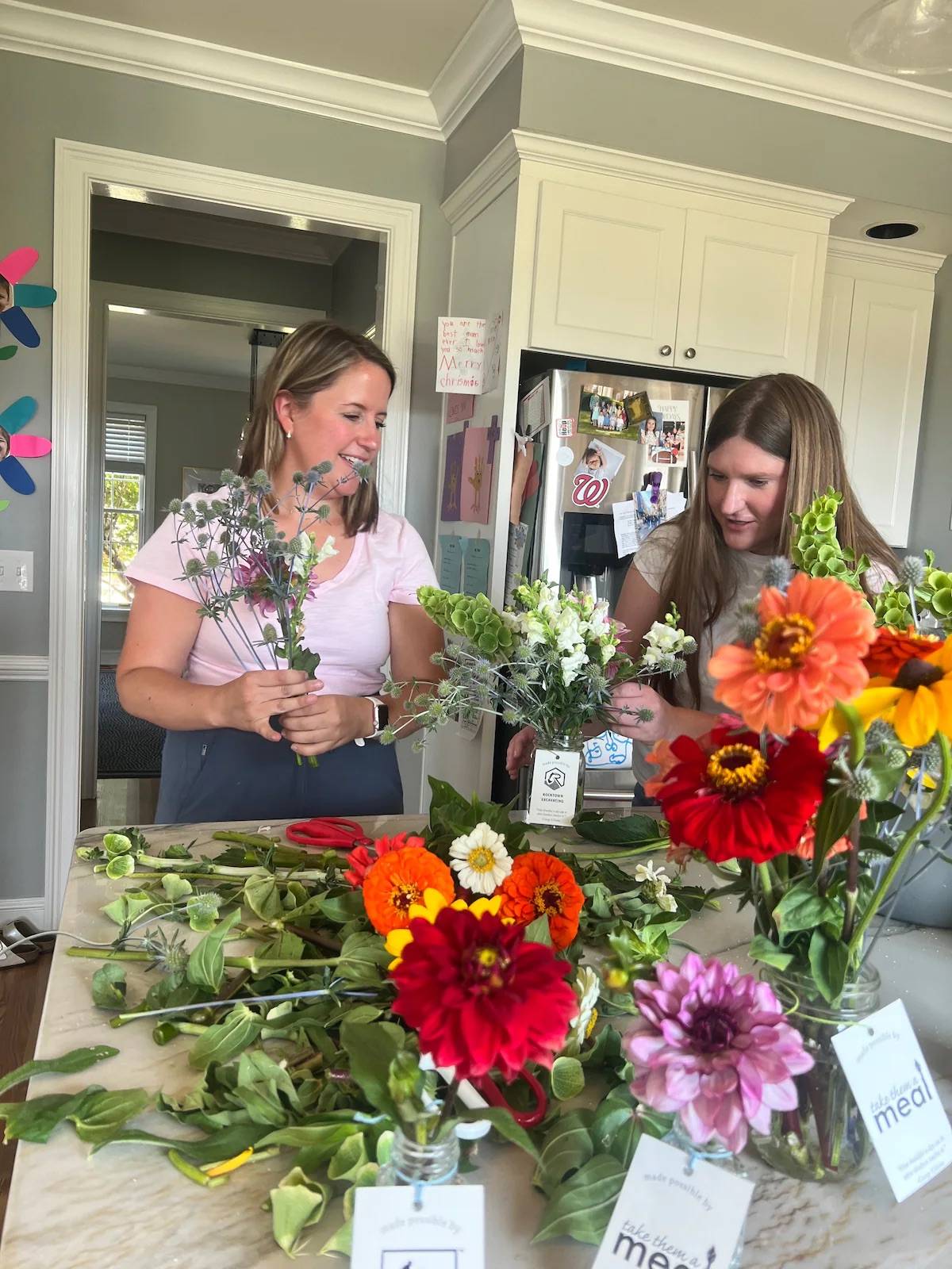 Two people standing at a kitchen island surrounded by flowers on the counter