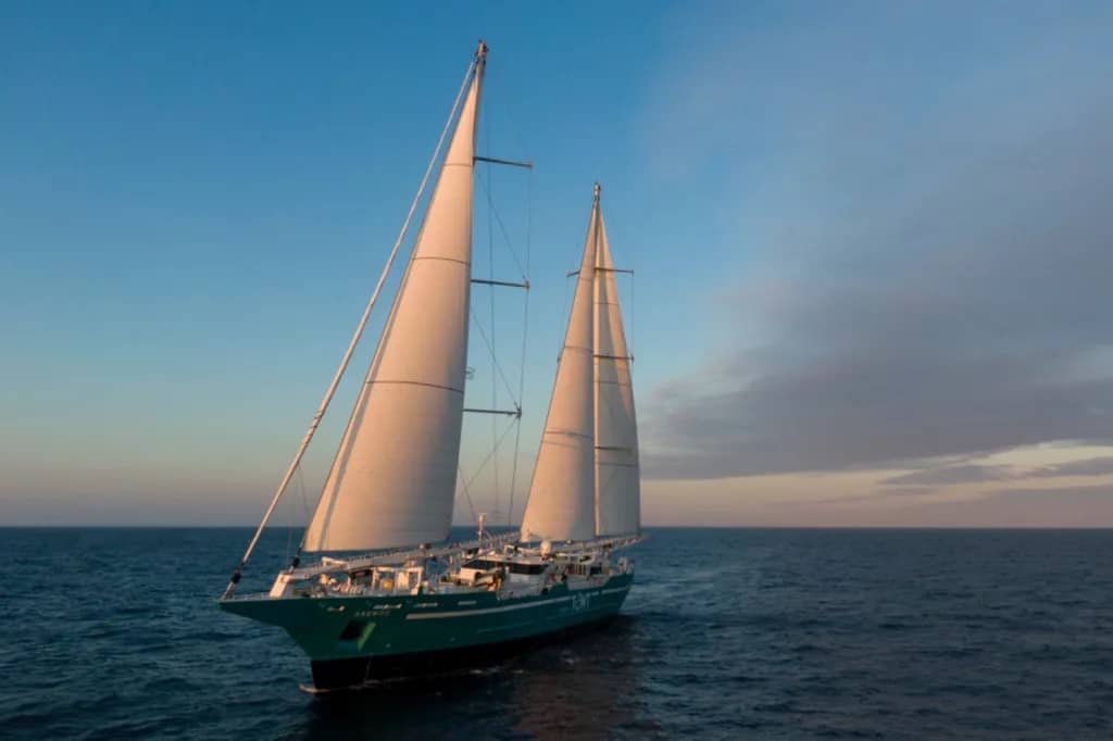 A ship with large white sails on the open sea with a fading blue sky in the background