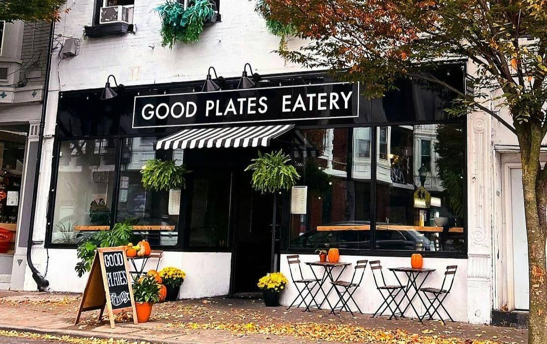 Exterior of Good Plates Eatery, there are leaves on the sidewalk, and small bistro tables in front of large windows