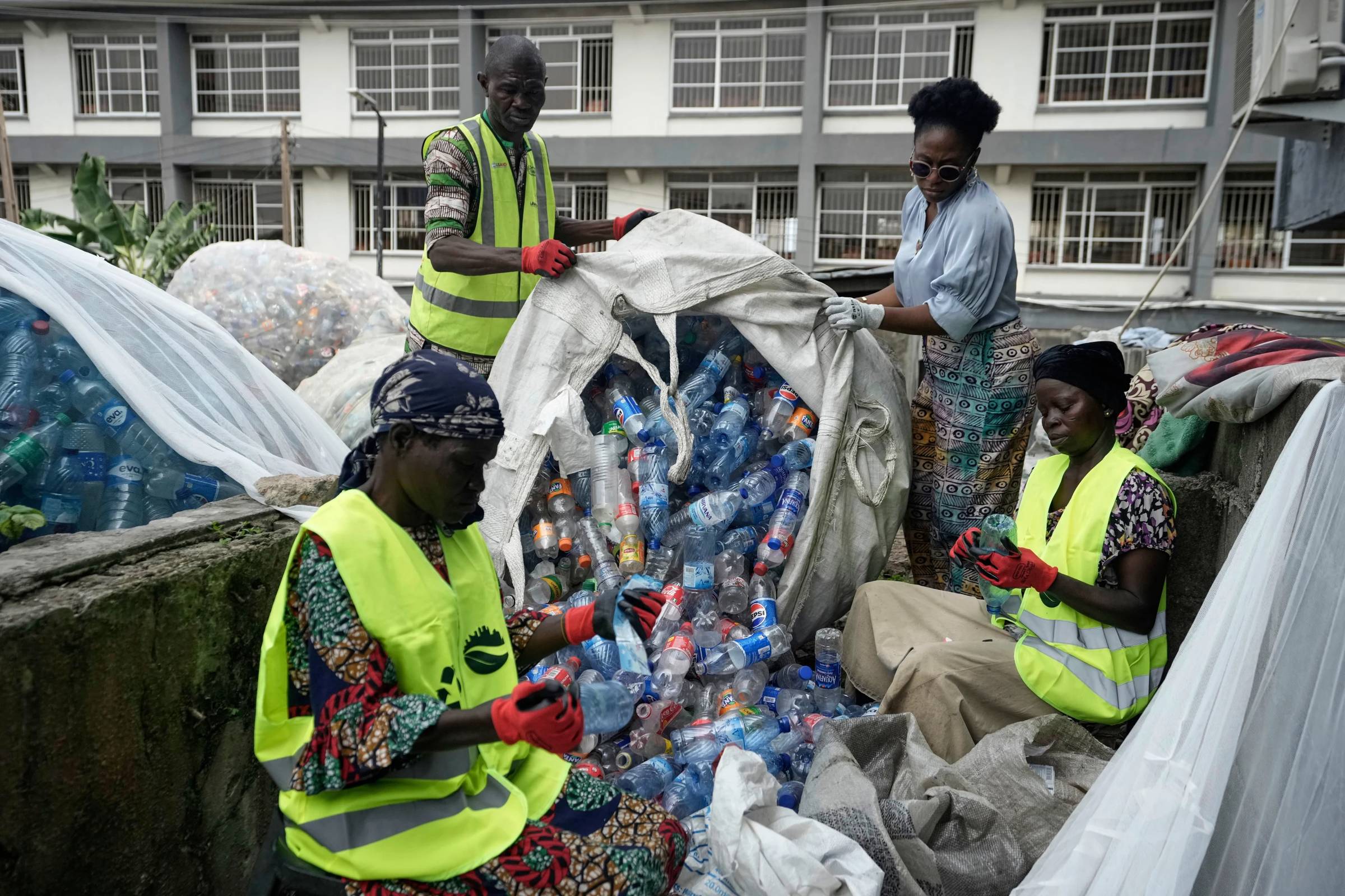 Two people emptying a bag of plastic bottles while two others scrape labels off them