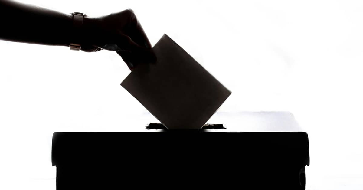 Silhouette of a hand putting a ballot into the top of a box