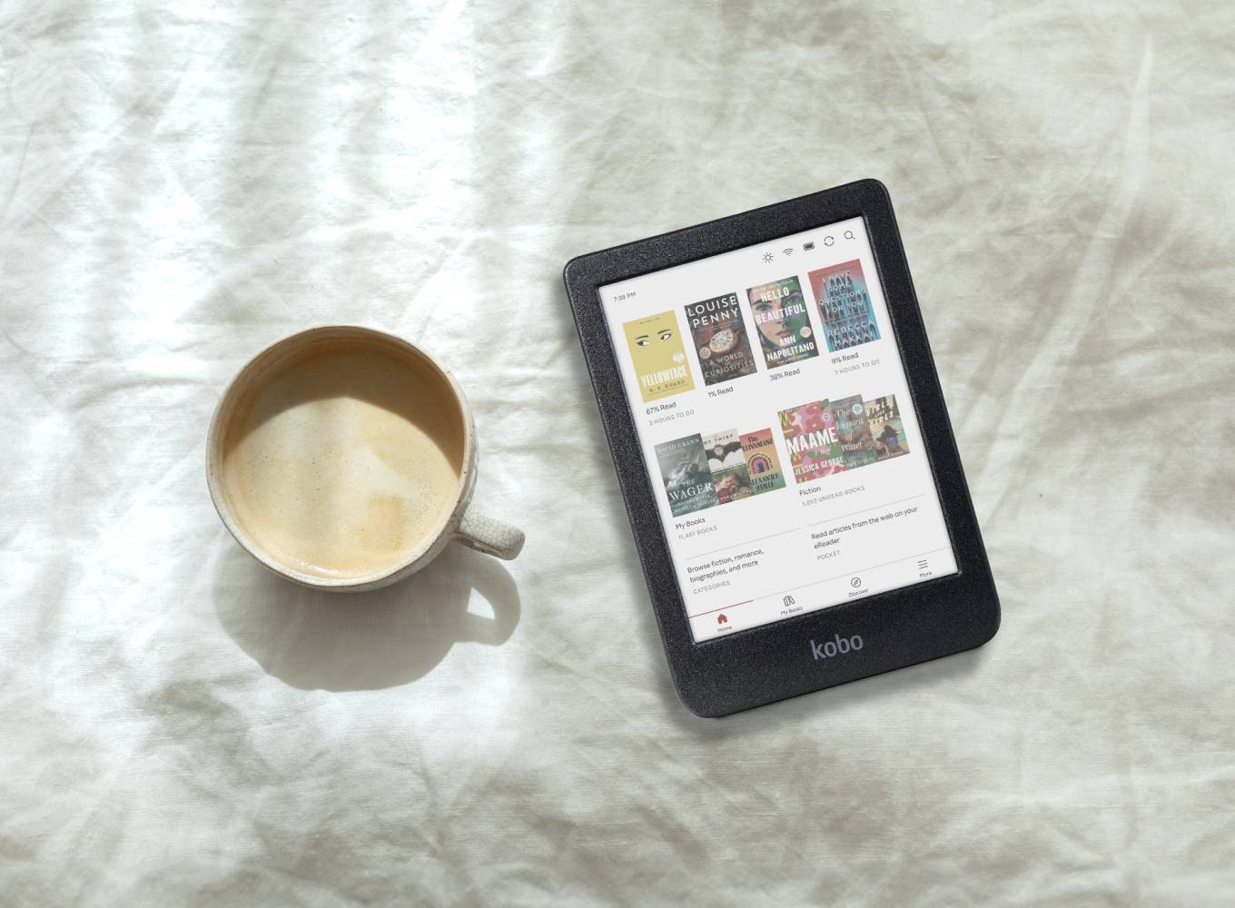 Overhead photo of a Kobo e-reader next to a coffee cup on white linen fabric