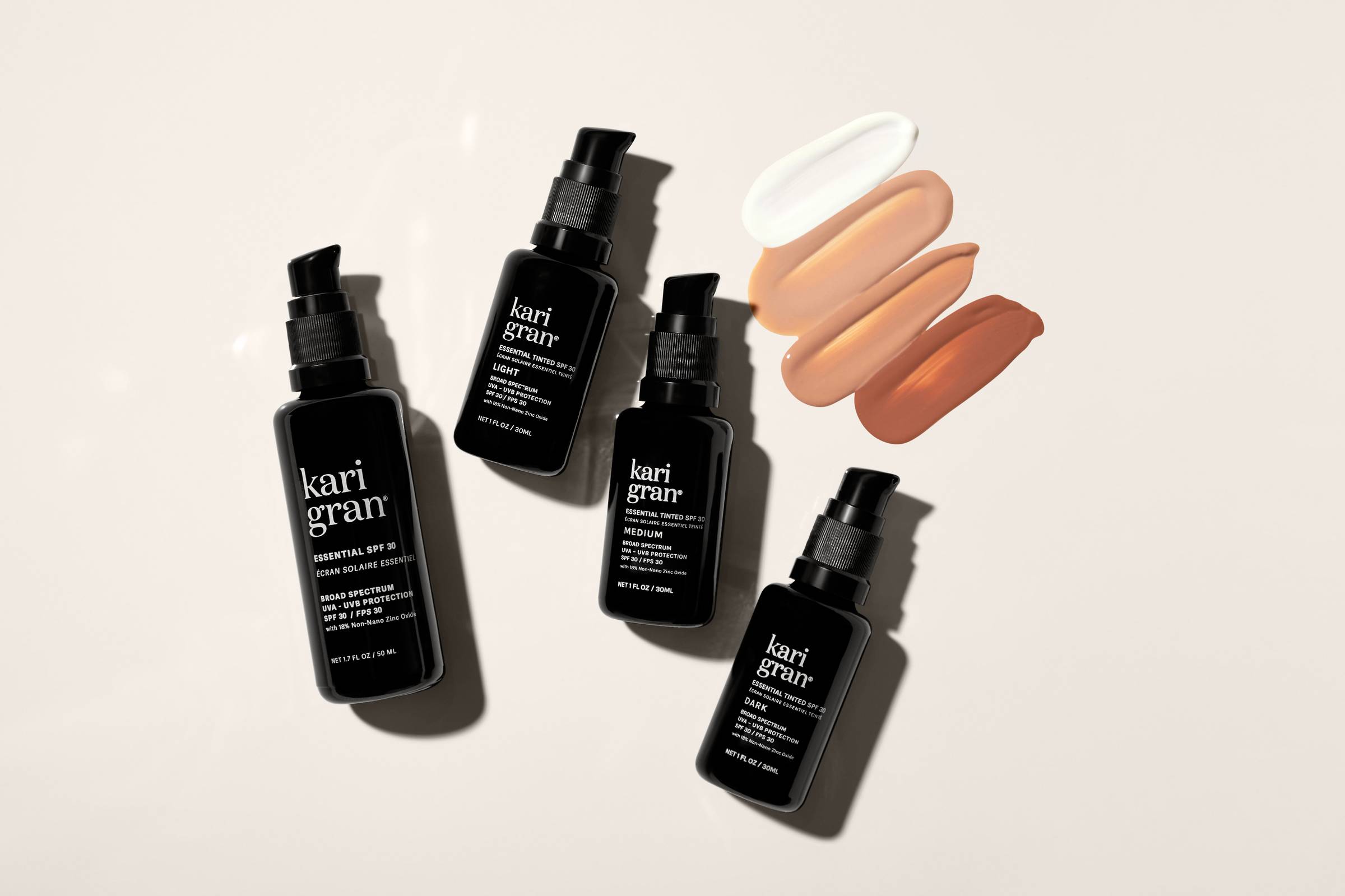 Four black pump-style skin care bottles with four swipes of white, and shades of tan on a beige background