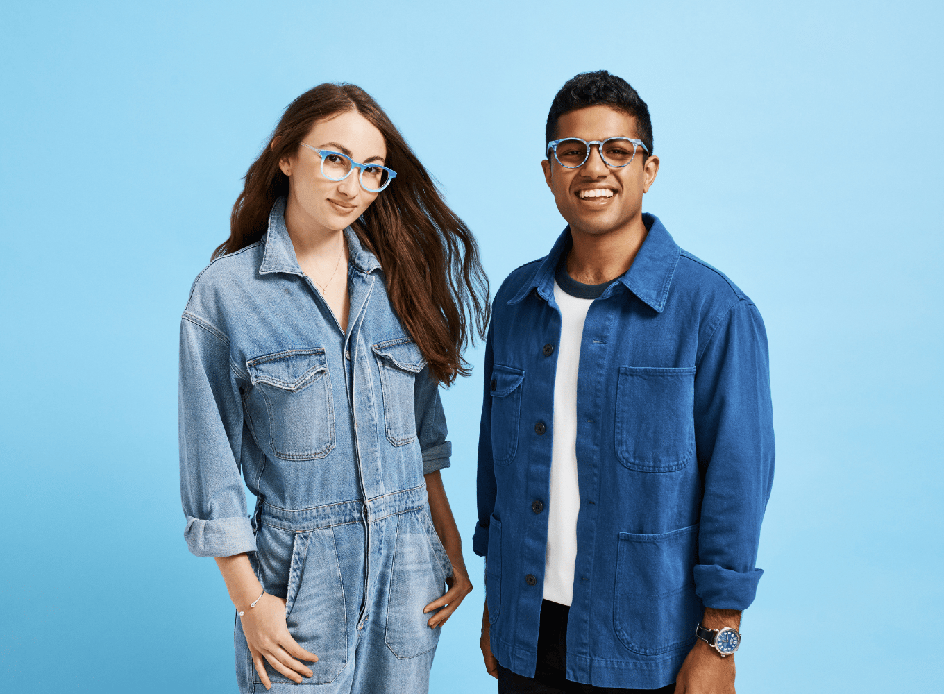 Pair Eyewear founders Sophia and Nathan wearing blue-colored glasses, denim outfits, standing on a blue background