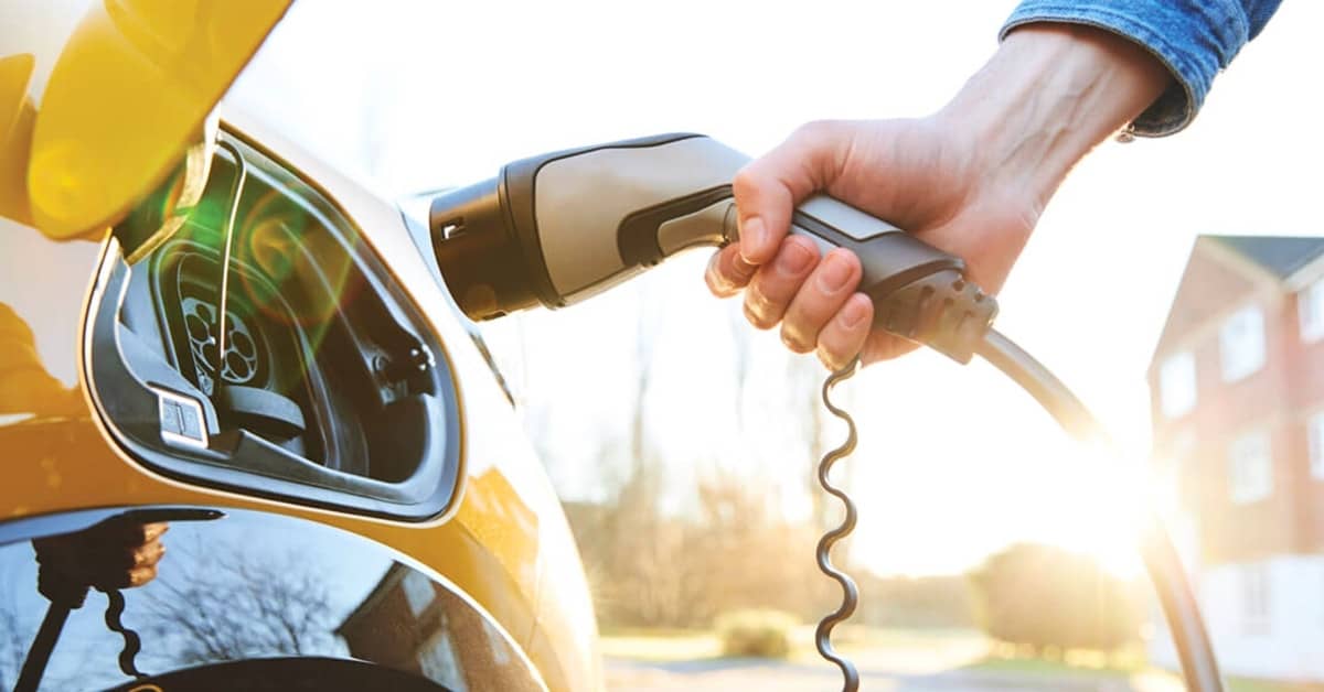 A hand holding an electric vehicle charger and putting it into the car