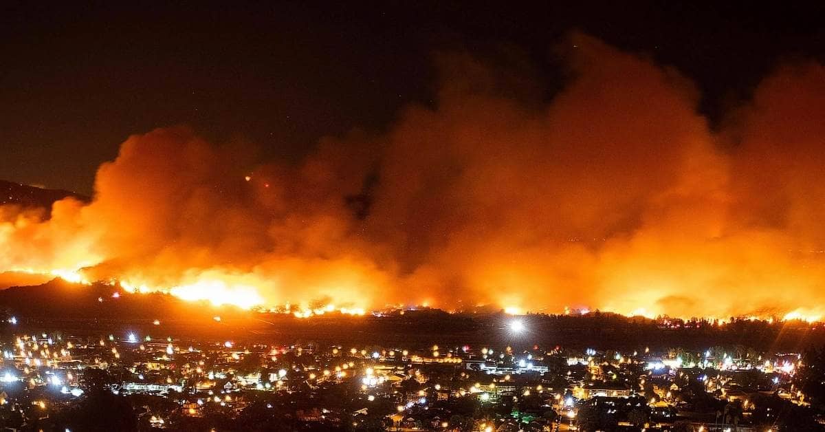 Wildfires blazing at night with a lit up neighborhood in the foreground