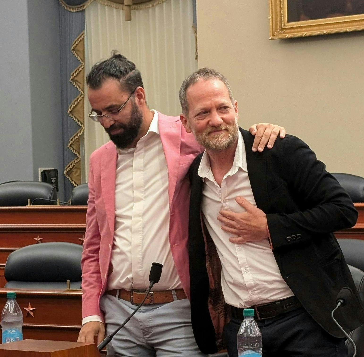 Maoz Inon and Aziz Abu Sarah stand in a congressional meeting room with their arms around each other
