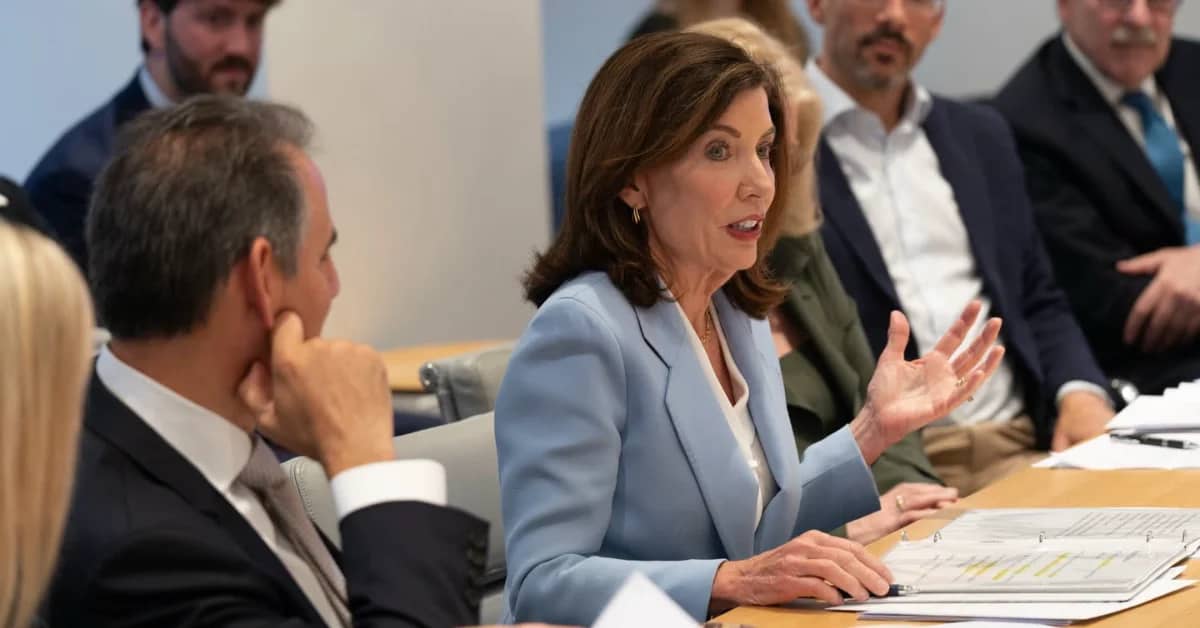 A woman wearing a light blue blazer sitting at a table talking to others around the table