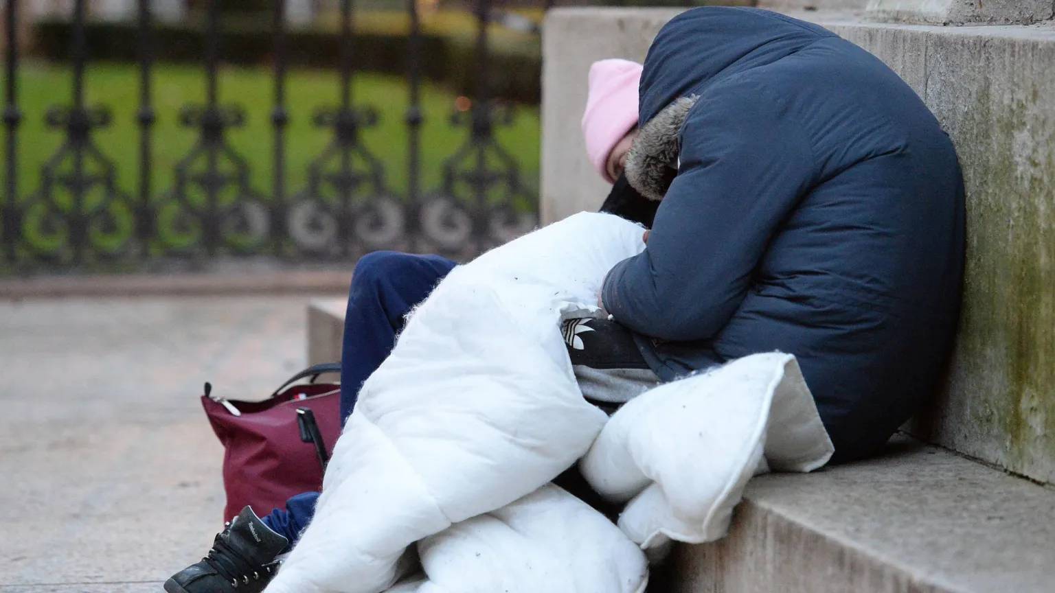 Two people leaned over sleeping on a concrete bench