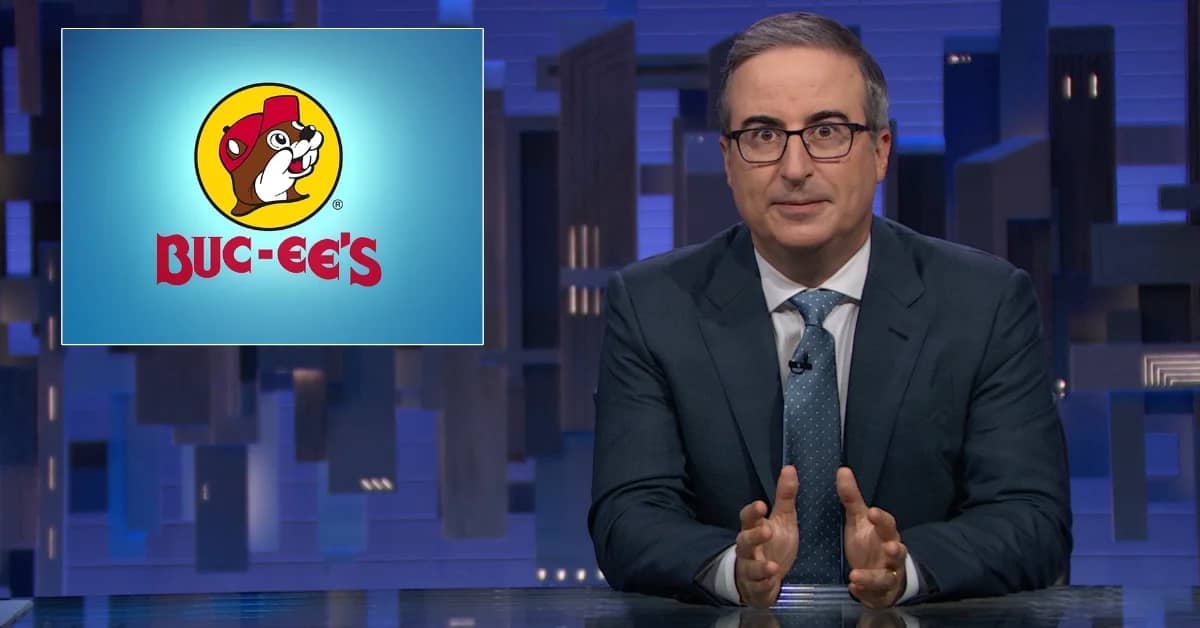 Man in dark suit and glasses sits at desk with cityscape backdrop, gesturing while speaking. Buc-ee's logo displayed on screen to his left.