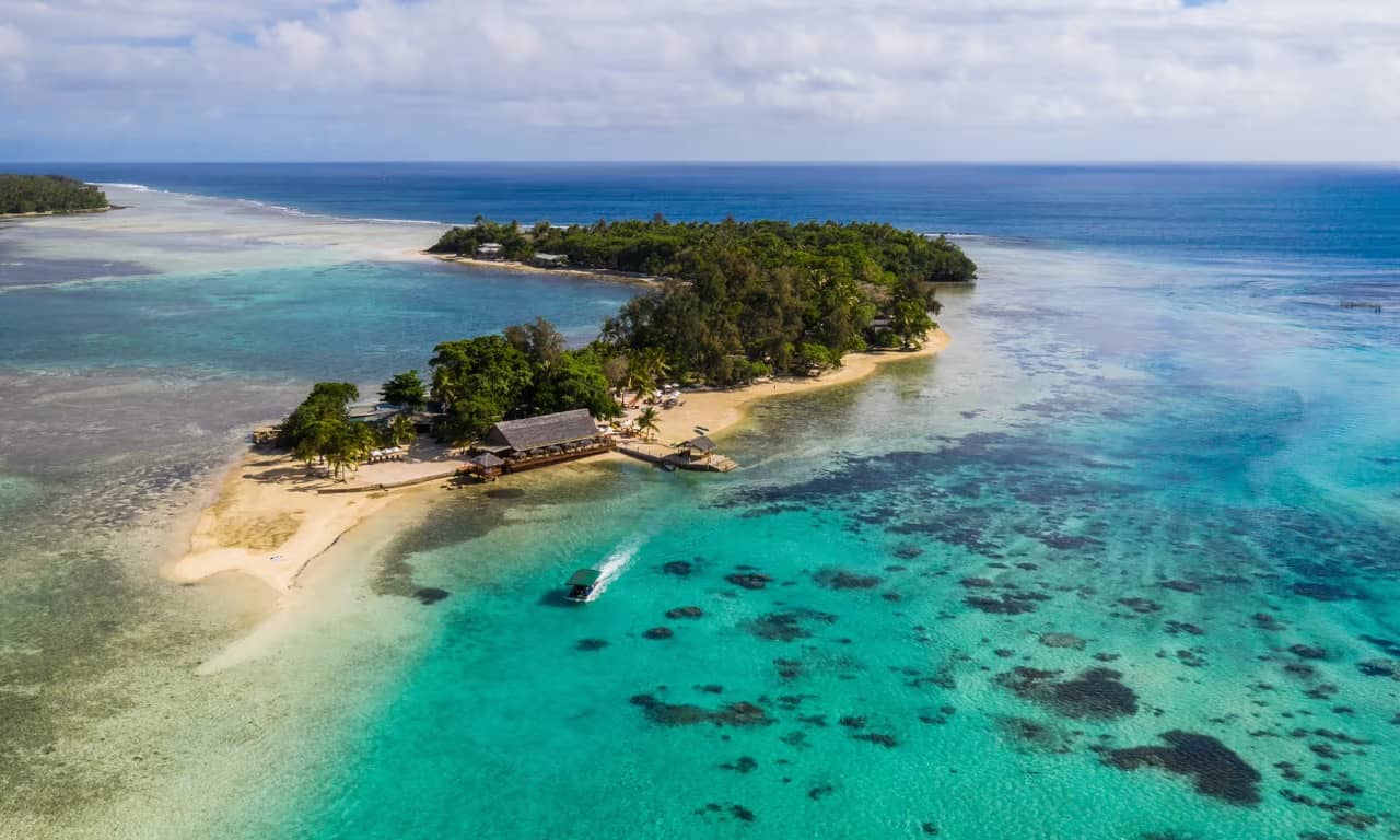 Aerial photo of a small, tree-filled sandy island surrounded by teal and blue waters