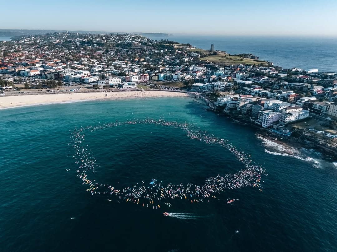 Drone-view of a massive circle of people on surfboards in the water
