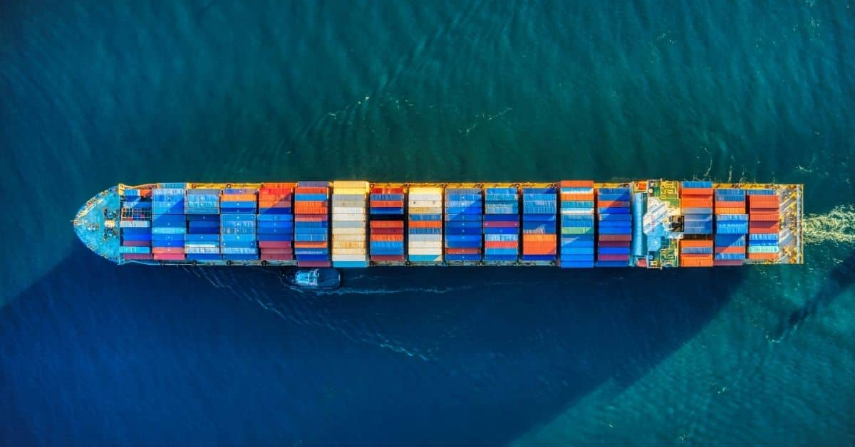 Aerial overhead photo of a cargo ship filled with shipping containers traveling over blue wate