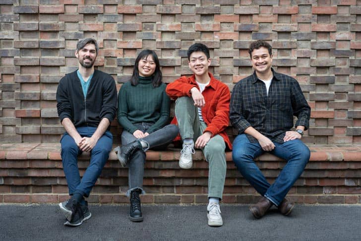 Four people sitting on a bench made from bricks with a brick wall behind them