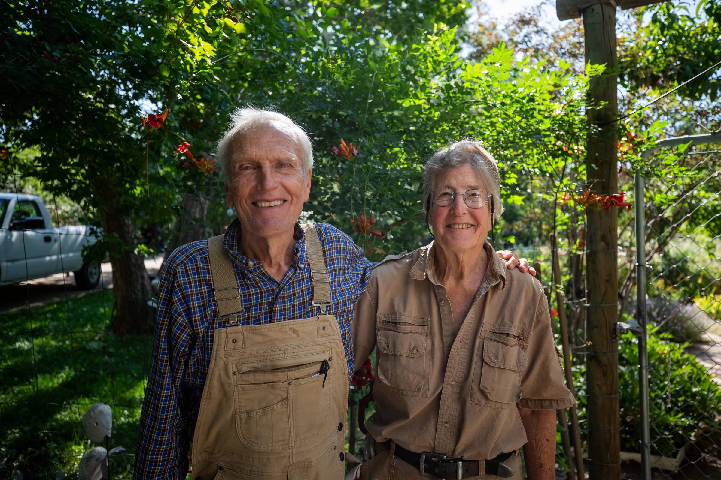 Two people with their arms around each other standing outdoors surrounded by trees