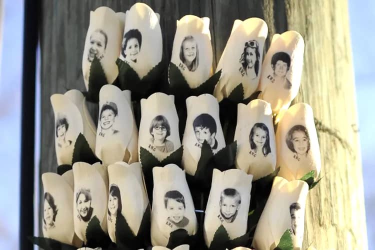 Seventeen white roses arranged in rows display black and white portrait photographs of people's faces printed on them.