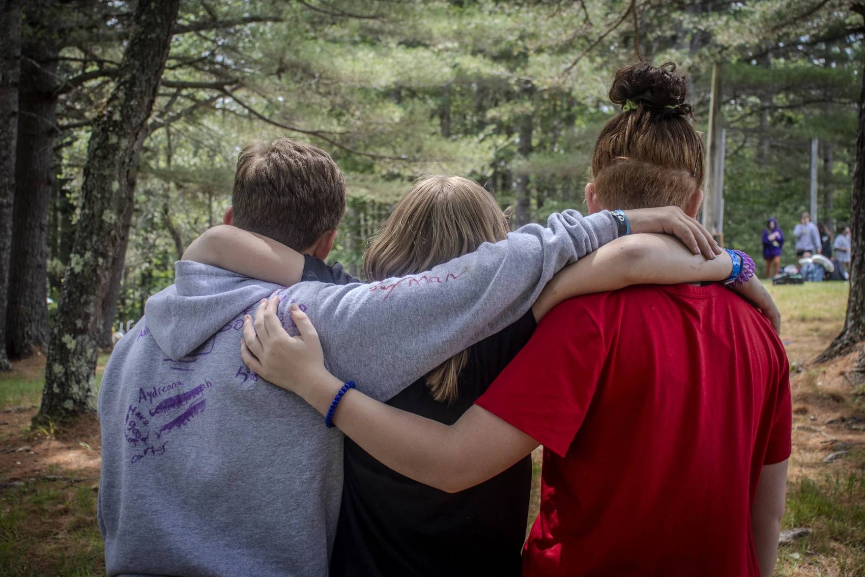 Three people with their arms around each other facing away from the camera