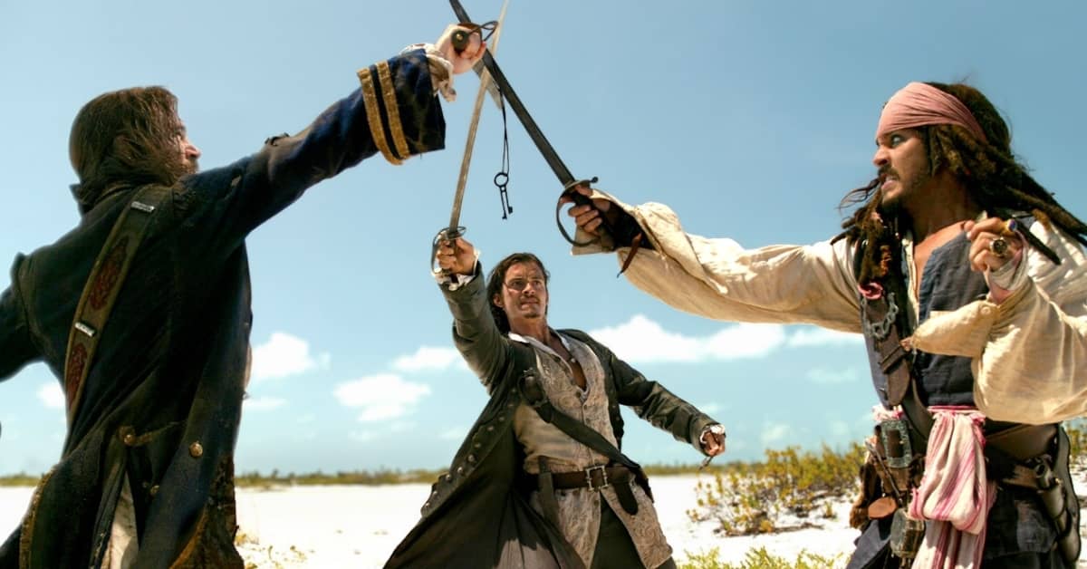 Still from Pirates of the Caribbean, three actors are fighting on a beach with their swords