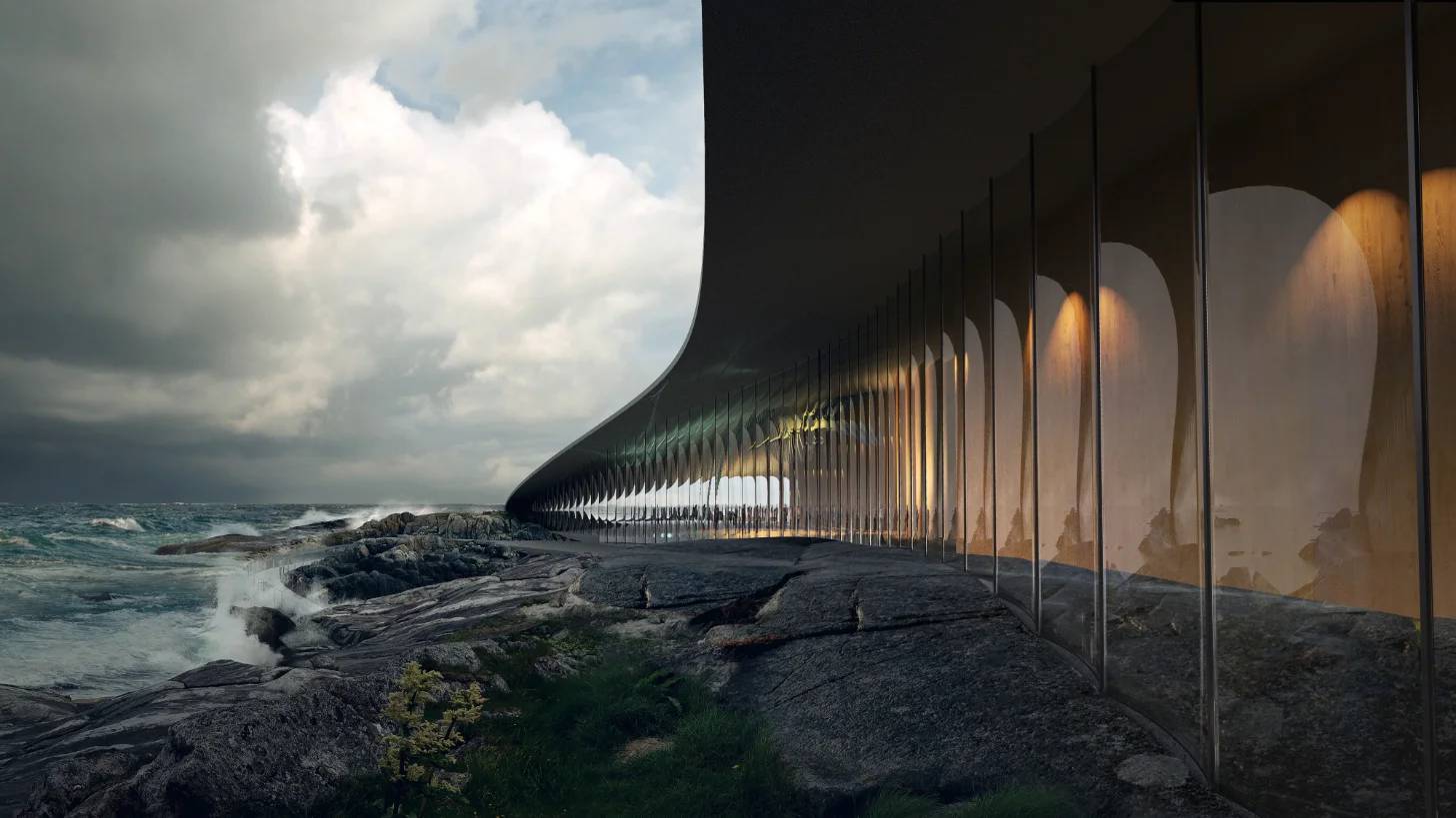 A modern structure with vertical metal columns and curved translucent panels stands on rocky coastline beside ocean waves, with cloudy sky and distant hills visible.