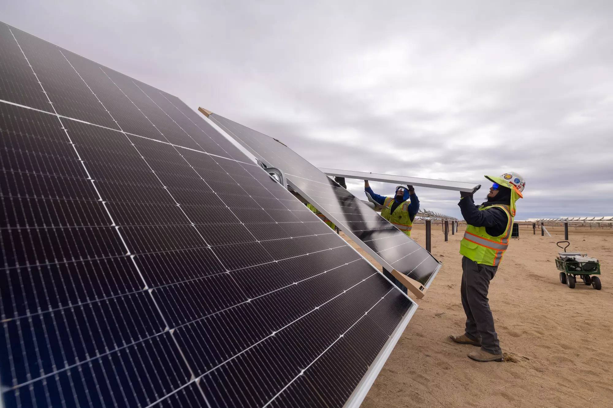 Two people installing a solar panel in a sandy area
