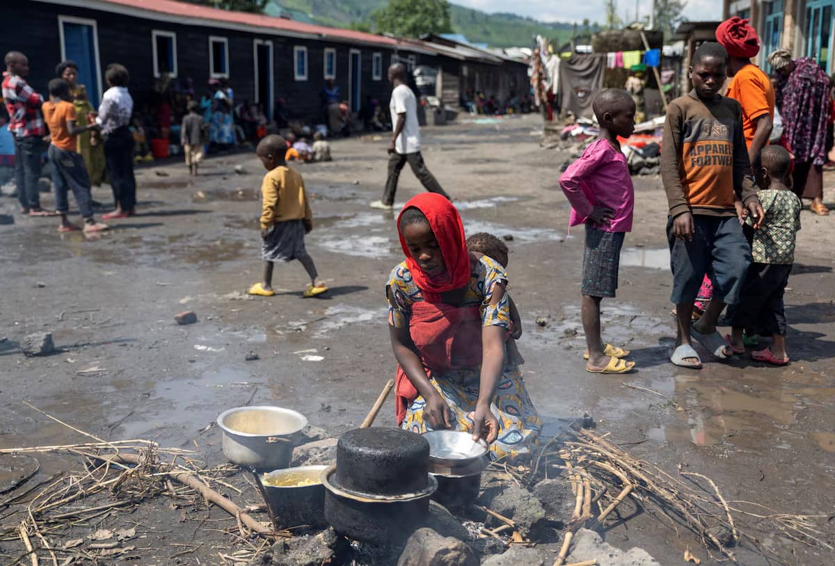 A woman with a red head scarf holding a baby prepares a meal at a primary school