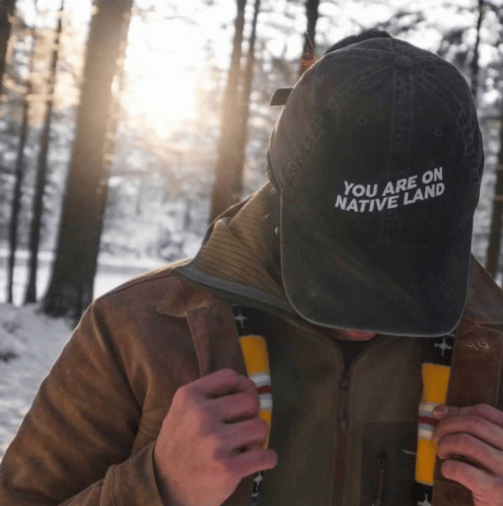 Person wearing a dad hat that says "You are on native land"
