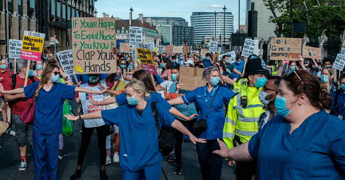 Nurses at a protest wearing blue scrubs and carrying signs