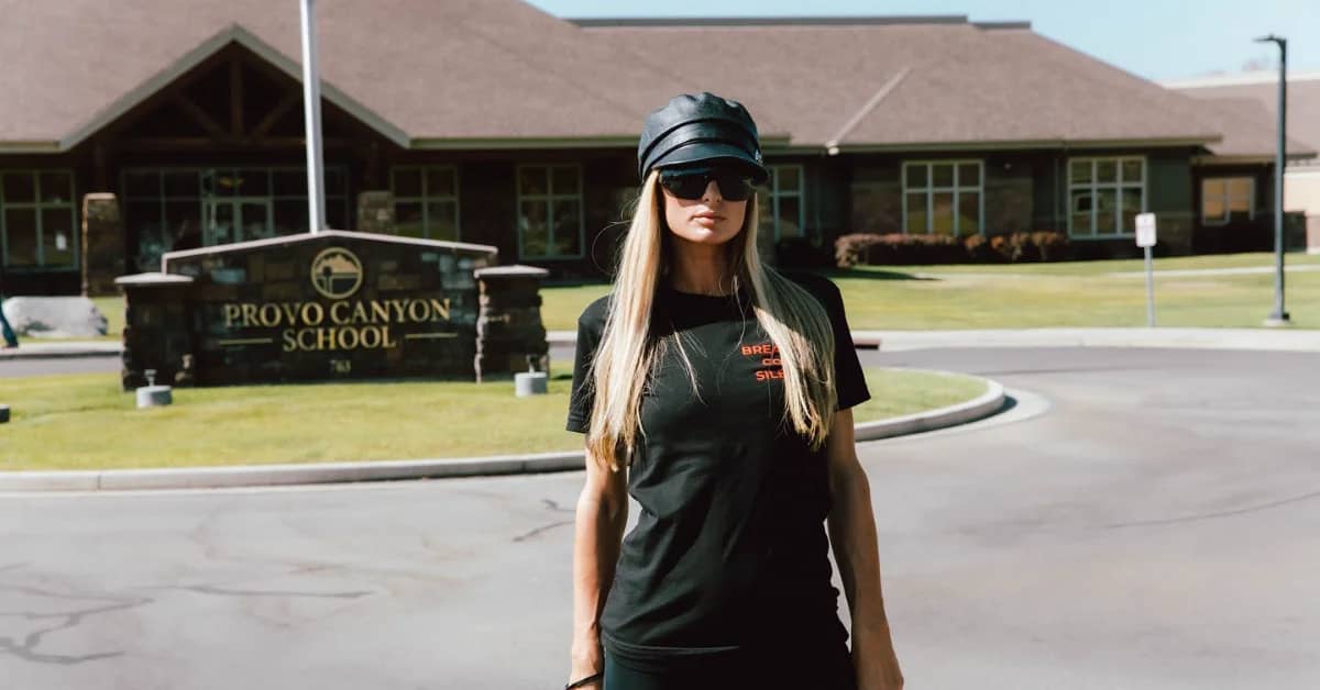 Paris Hilton standing in front of a sign for "Provo Canyon School"