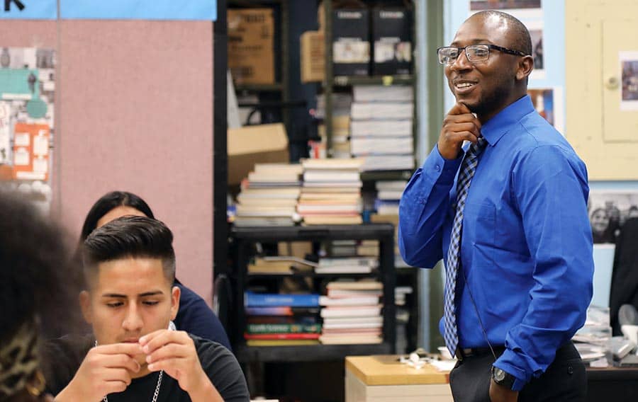 A teacher wearing a blue shirt and tie in a classroom
