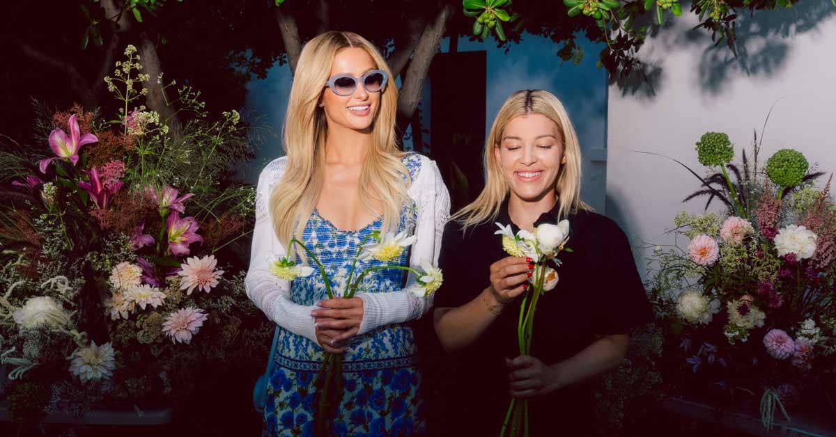 Paris Hilton and another person holding small bouquets of flowers with larger bouquets next to them