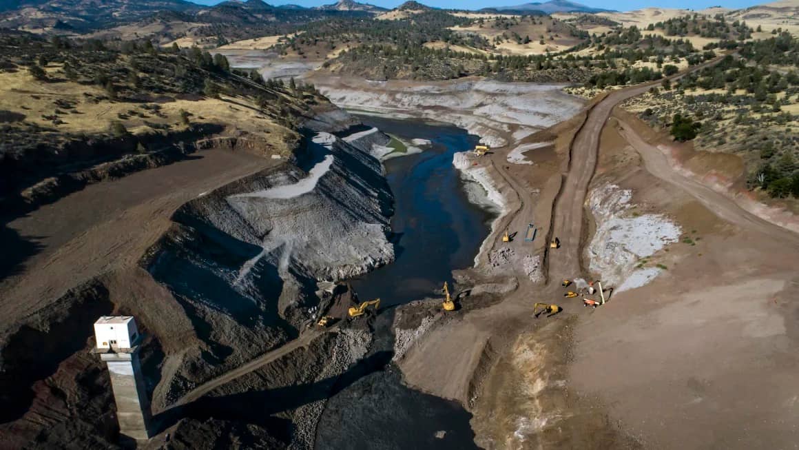 Aerial photo of the Klamath river flowing in its original path for the first time in a century with small construction vehicles visible on either side of the river