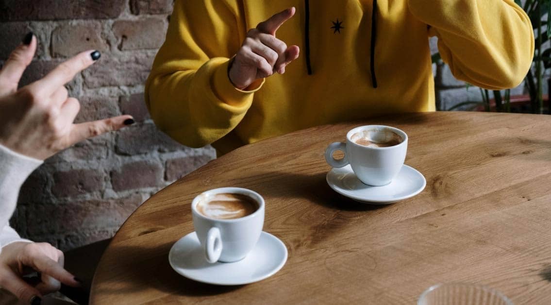 Two people at a table communicating in sign language with coffee cups in front of them
