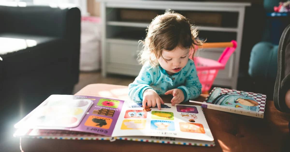 A small child reading a book on an ottoman